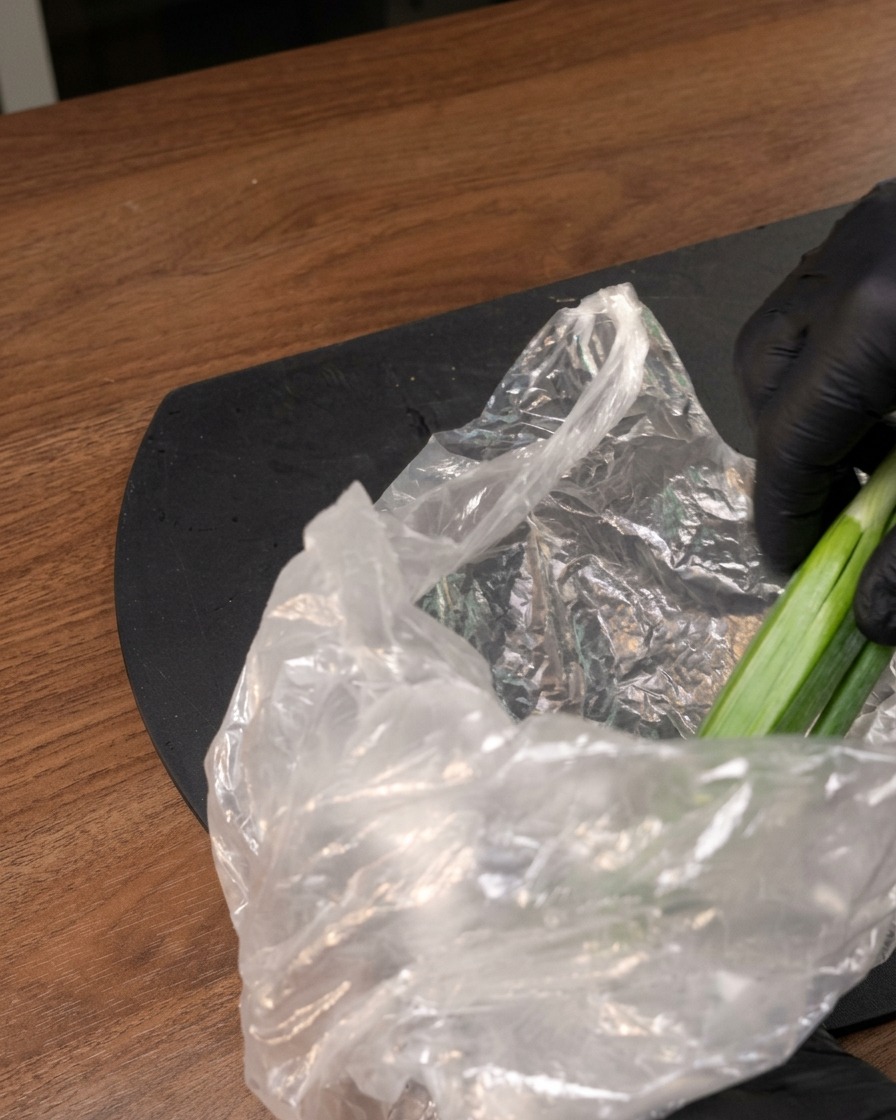 Une main gantée sortant des gombos frais dun sachet plastique sur un plan de travail sombre.