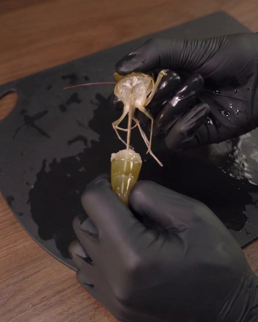 Une personne avec des gants noirs retirant la tête dune crevette crue.