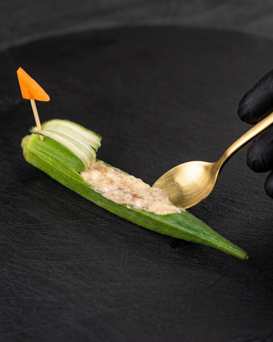 Une petite cuillère dorée remplissant un gombo évidé avec la farce de crevettes.