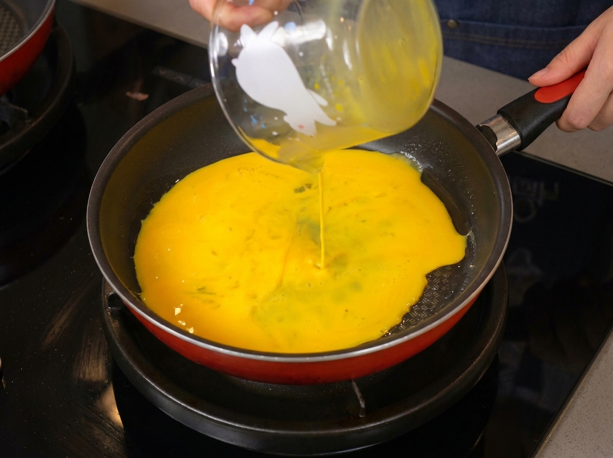 Œufs battus jaune vif versés dun verre doseur dans une poêle chaude.