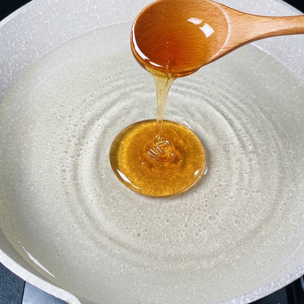 Une cuillère en bois versant un filet dhuile de cuisson dorée dans une casserole deau chaude.
