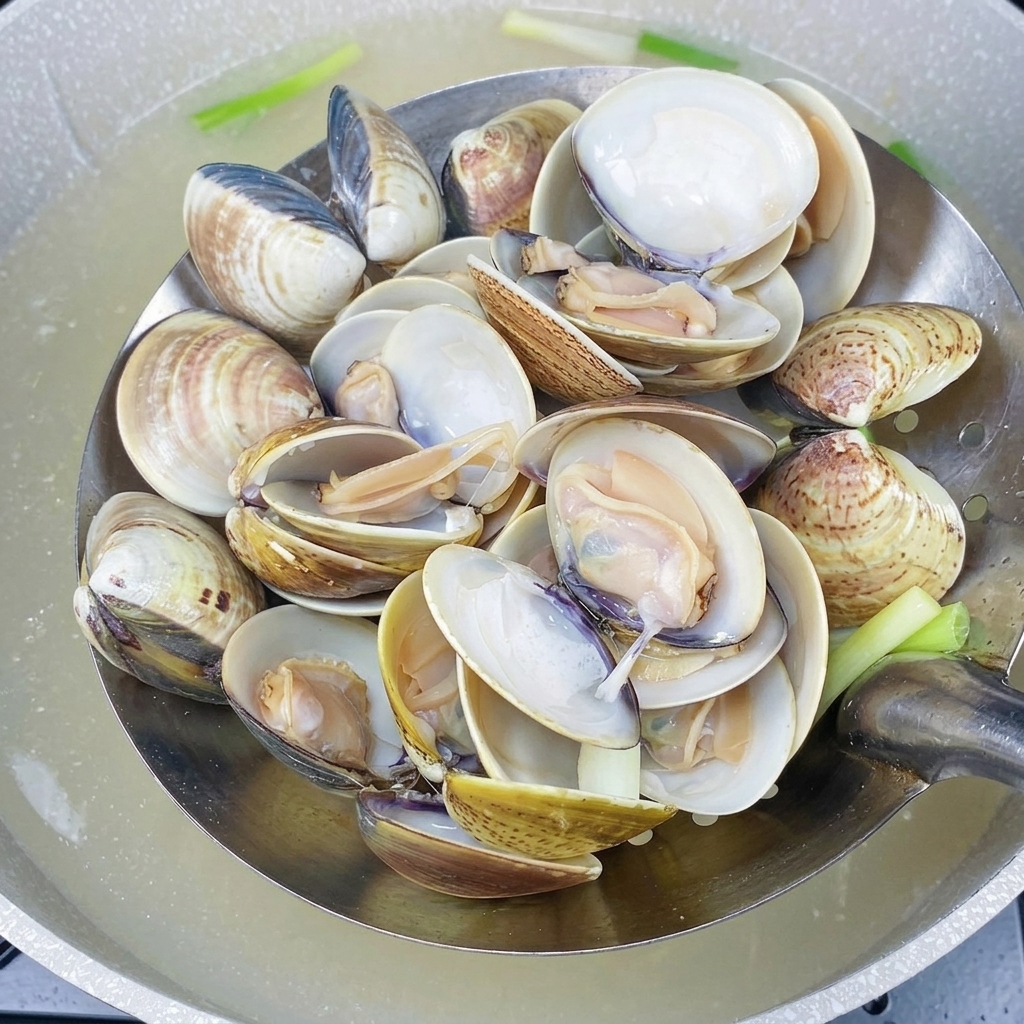 Une écumoire en métal tenant des palourdes cuites avec des coquilles bien ouvertes, sorties de leau bouillante.