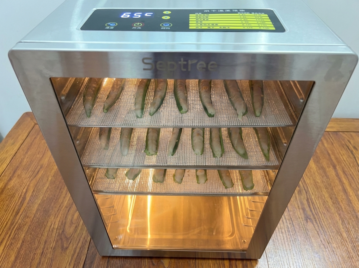 Plateaux chargés de gombos farcis glissés dans un déshydrateur en inox.