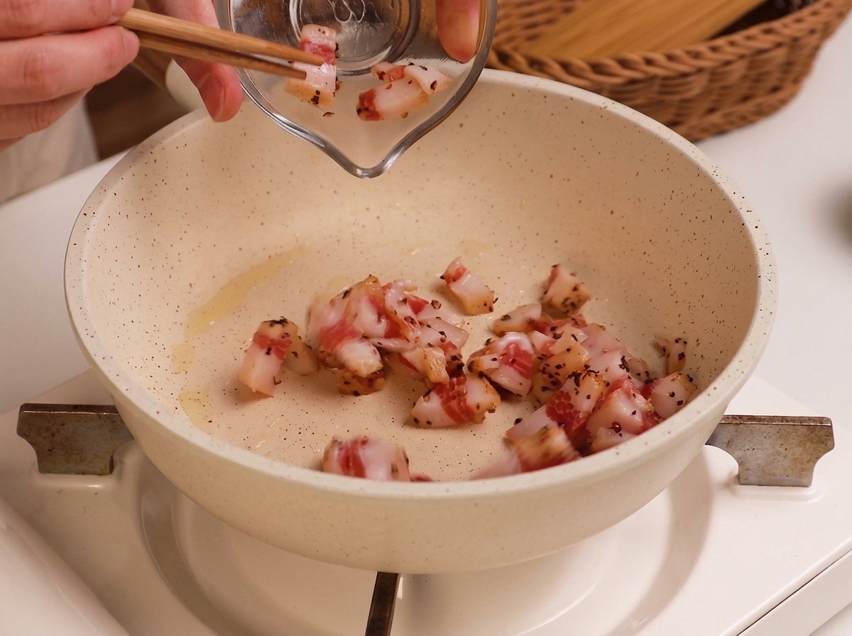 Dés de guanciale cru versés dans une poêle blanche légèrement huilée.