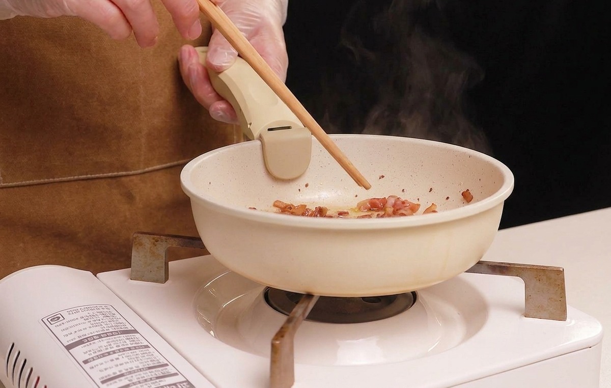 Mélange du guanciale avec des baguettes dans une poêle pendant quil dore.