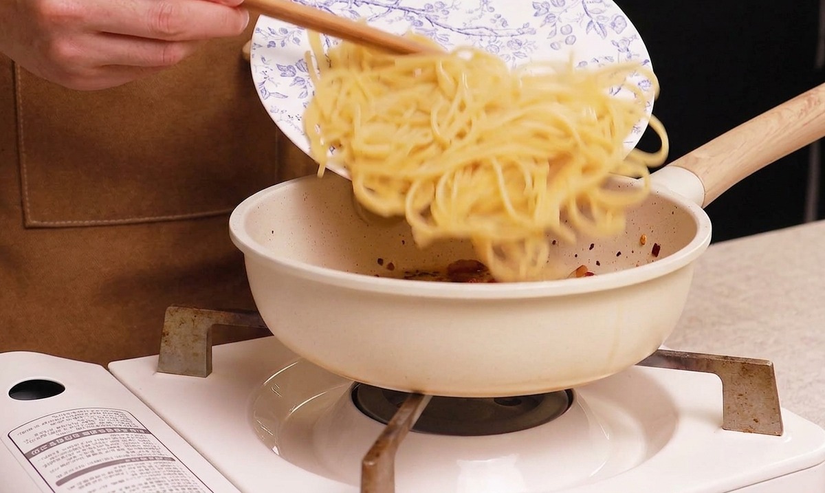 Spaghetti cuits glissant dune assiette vers une poêle contenant le guanciale croustillant.