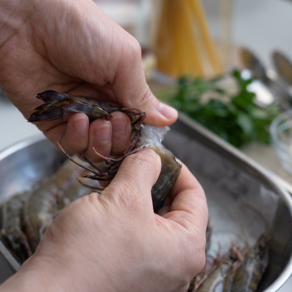 Mains décortiquant une crevette tigrée crue au-dessus dun bol en inox, en gardant la tête.