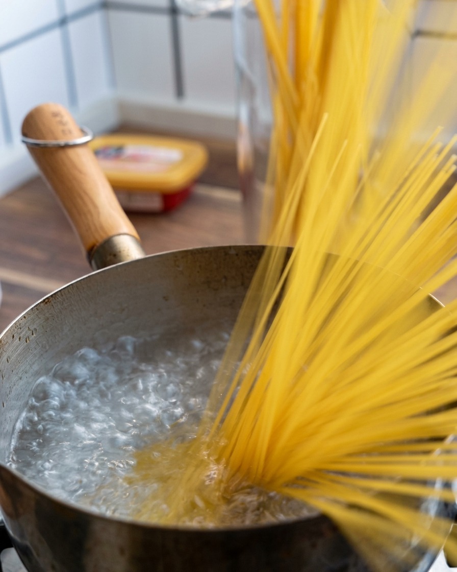 Une poignée de spaghettis secs plongée dans une casserole deau bouillante.
