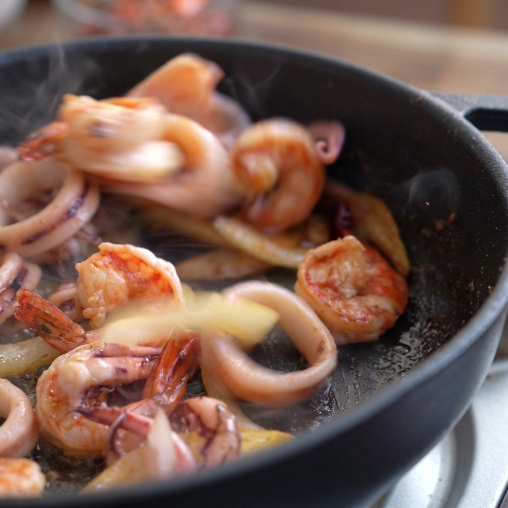 Crevettes et calamar sautant vivement dans la poêle, les crevettes commençant à rosir.