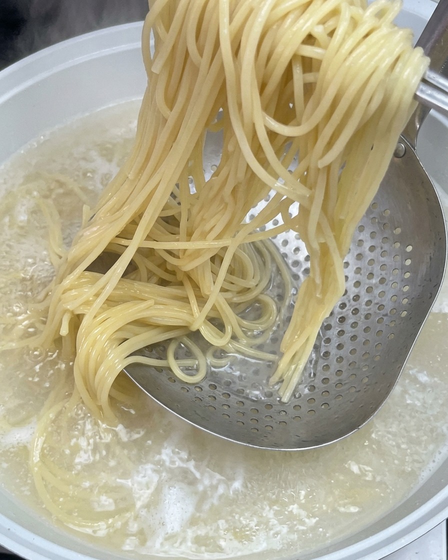Spaghetti cuits sortis de leau bouillante à laide dune écumoire métallique.