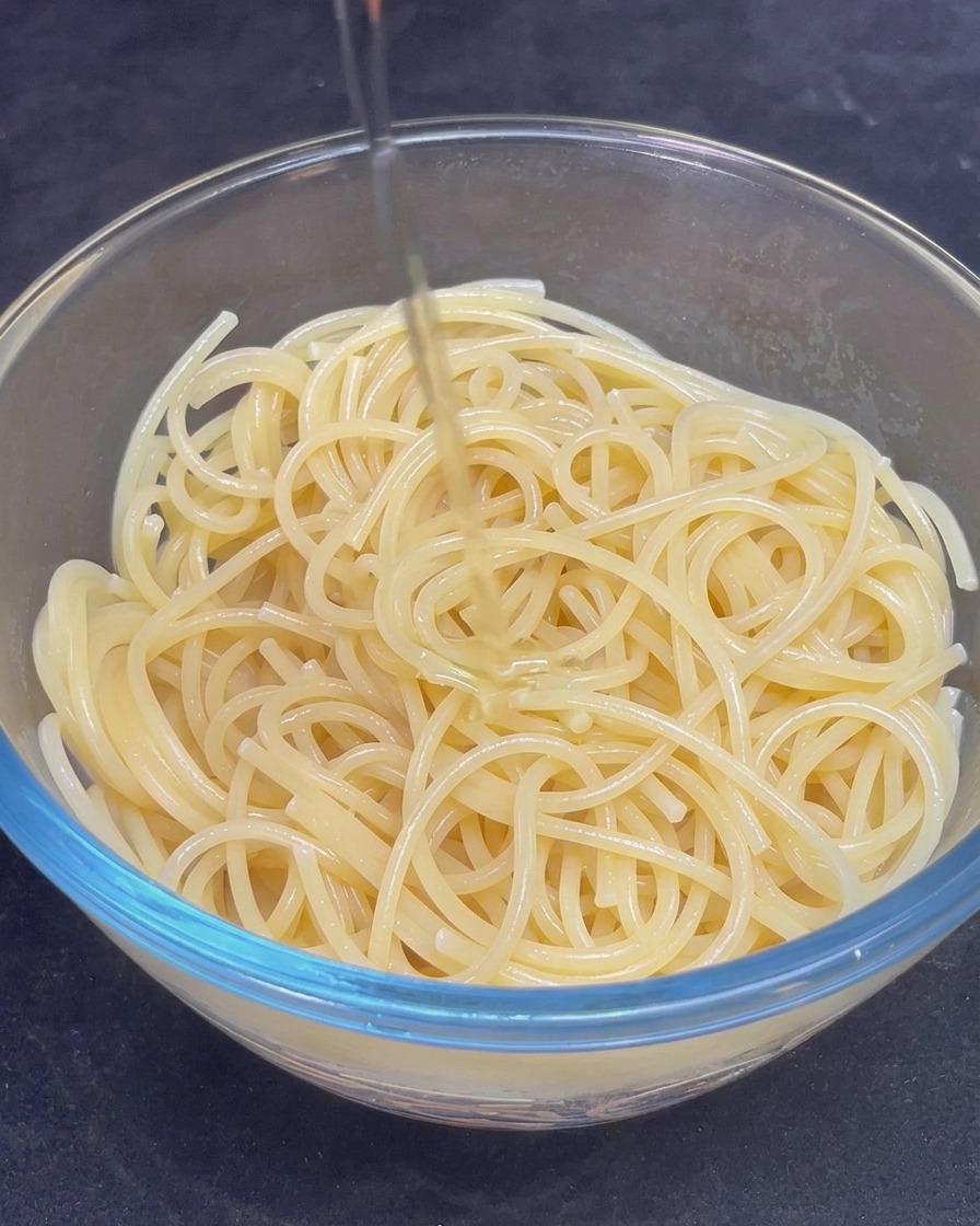 Filet dhuile dolive dorée versé sur les spaghetti cuits dans un bol en verre.