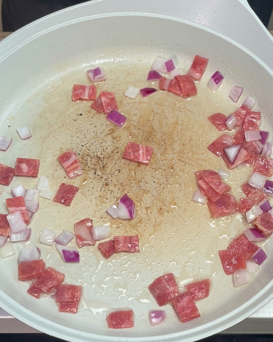 Poivre noir moulu saupoudré sur le mélange bacon et oignons en cours de cuisson.
