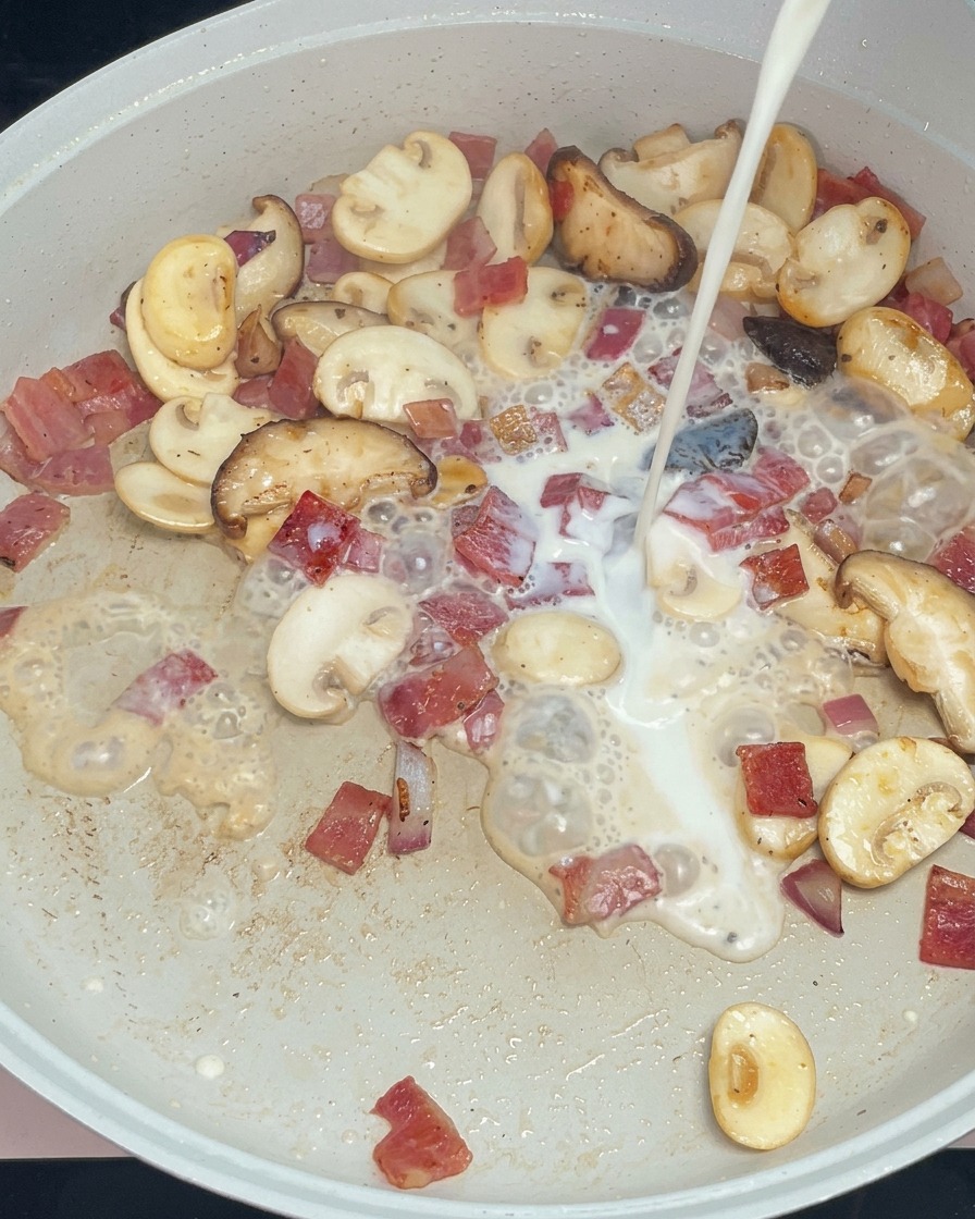 Lait blanc versé sur la garniture de champignons et bacon dans la poêle.