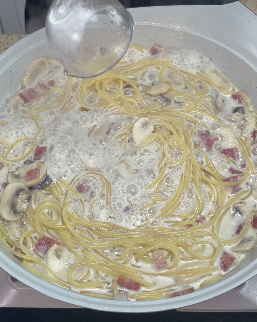 Cuillère en bois mélangeant les spaghetti avec du fromage fondu et lassaisonnement dans la poêle.