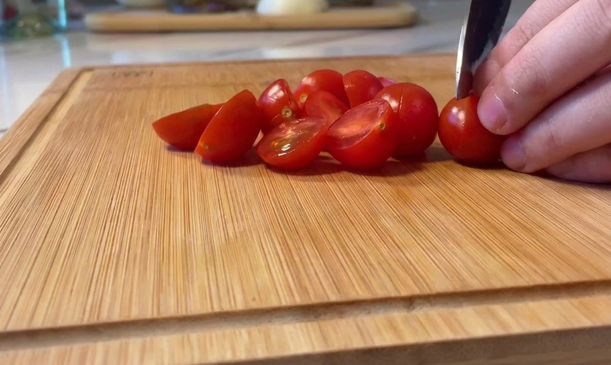 Couper des tomates cerises rouges bien mûres en deux sur une planche à découper.