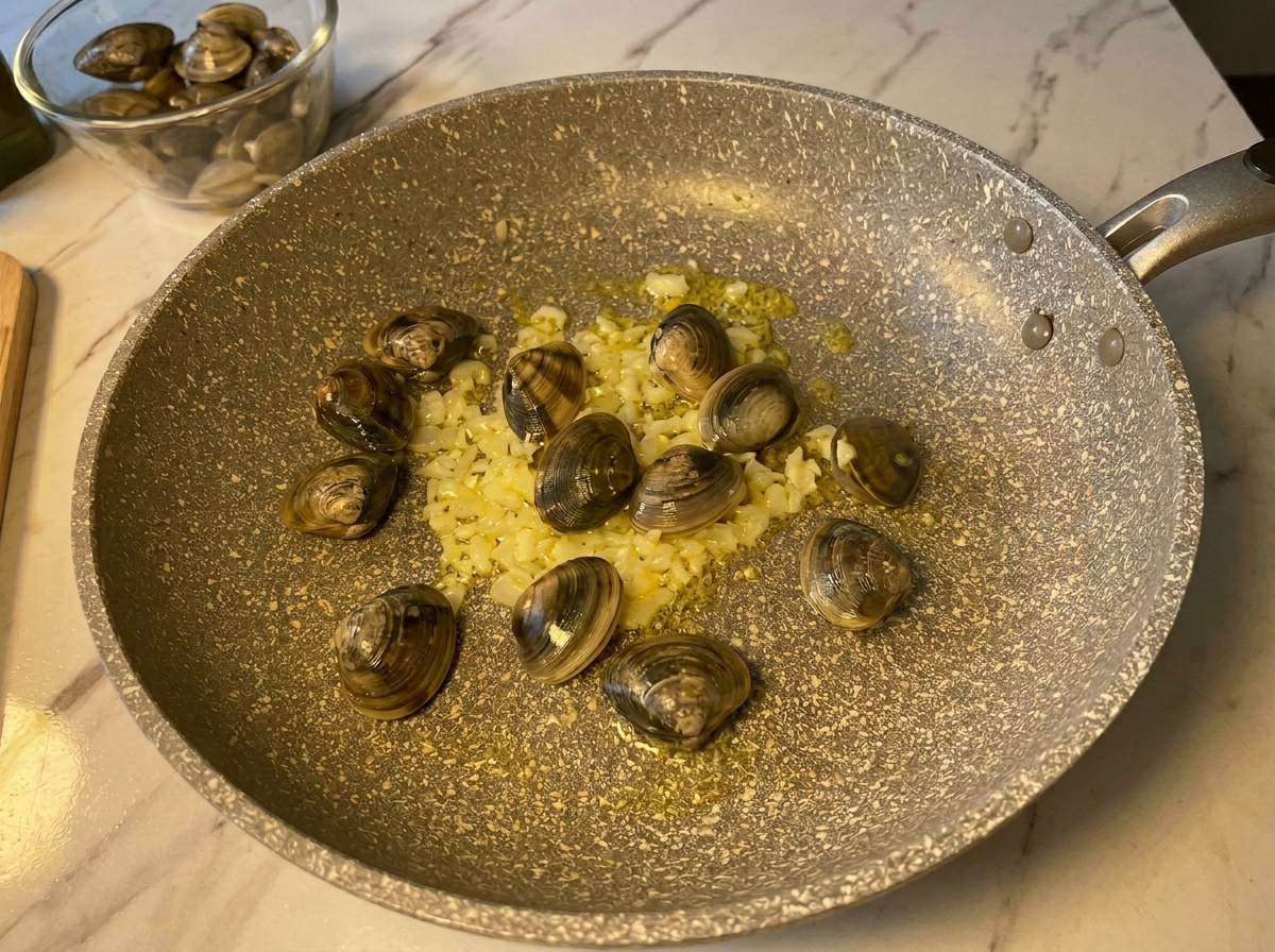 Palourdes fraîches fermées ajoutées dans la poêle chaude avec lail et loignon sautés.