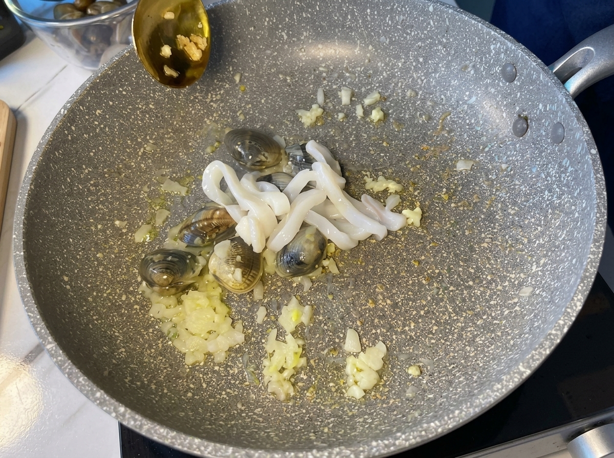 Anneaux de calamar blancs crus ajoutés dans la poêle contenant les palourdes et les aromates.