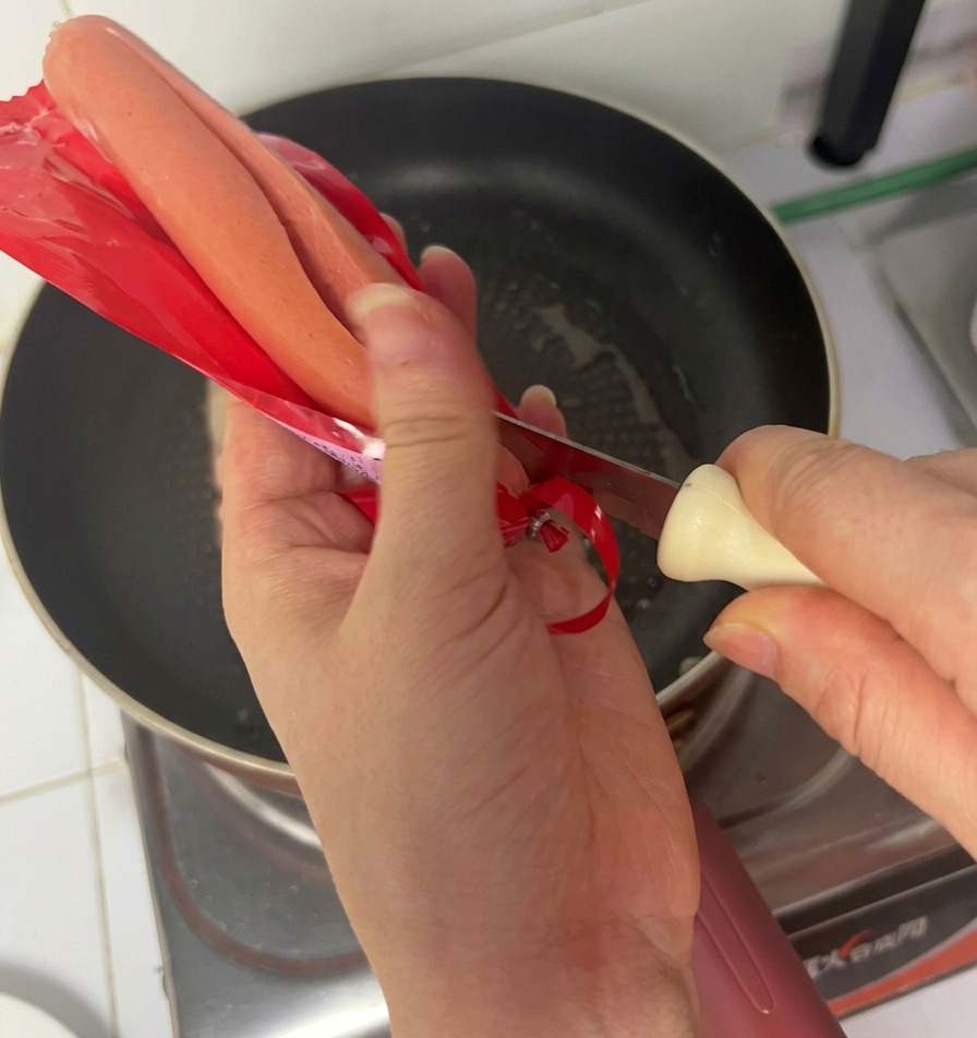 Mains déballant une saucisse de jambon au-dessus de la poêle contenant le bacon.