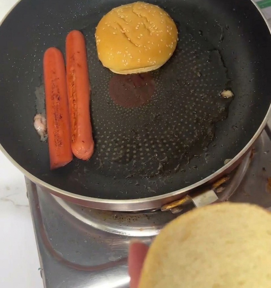 Pains burger au sésame posés face coupée contre la poêle à côté des tranches de jambon.