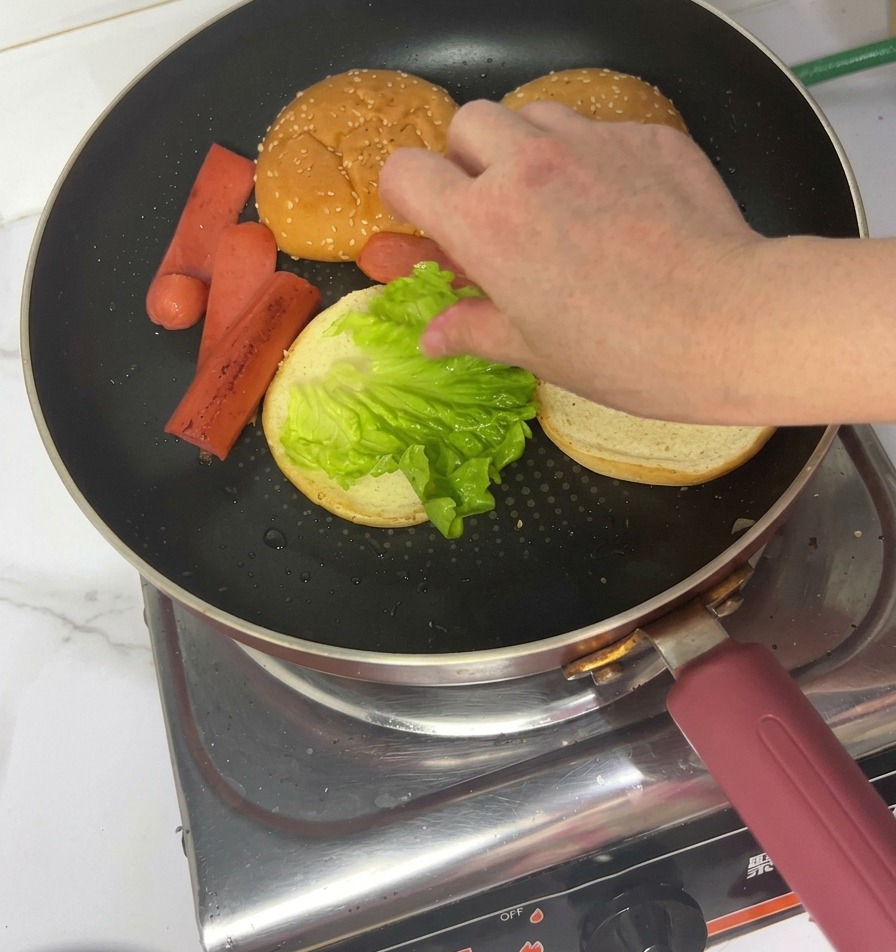 Une main déposant une feuille de laitue fraîche sur un pain toasté dans la poêle.