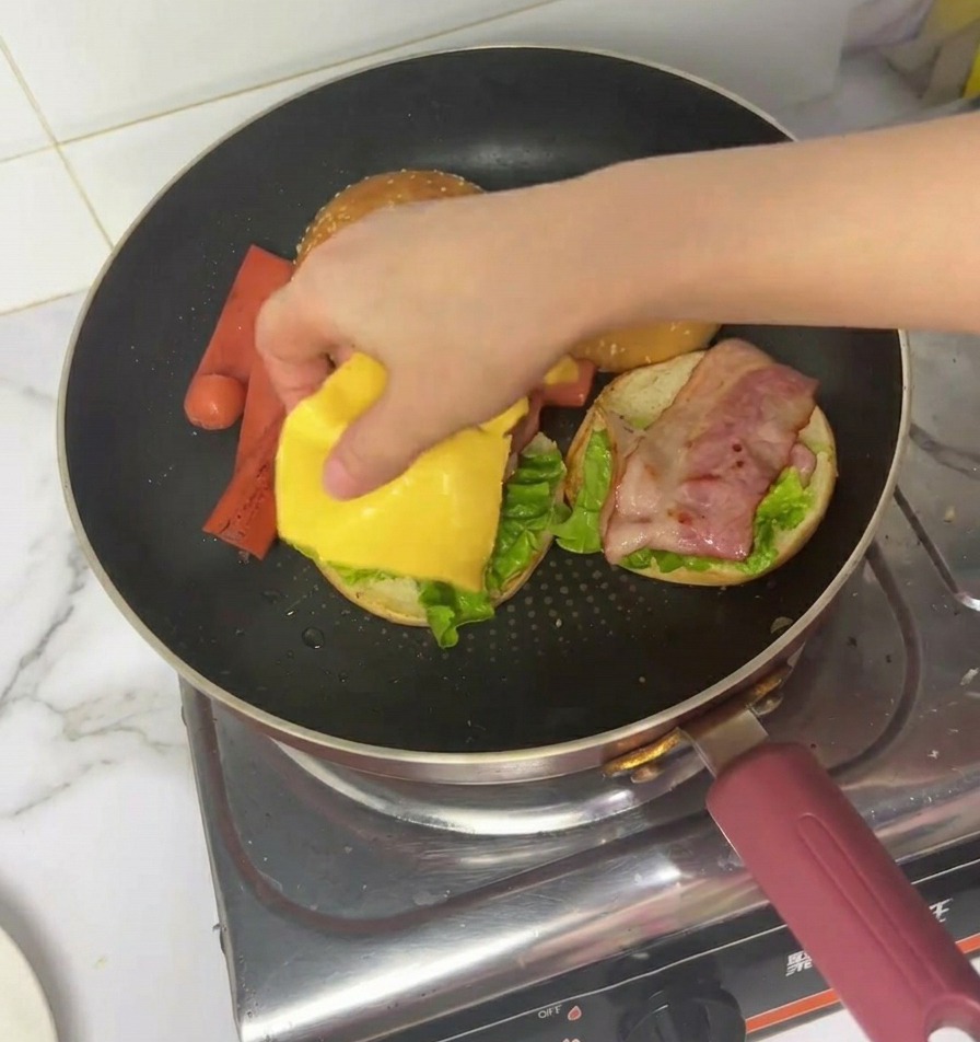 Une main plaçant une tranche de fromage jaune sur le bacon et la laitue.