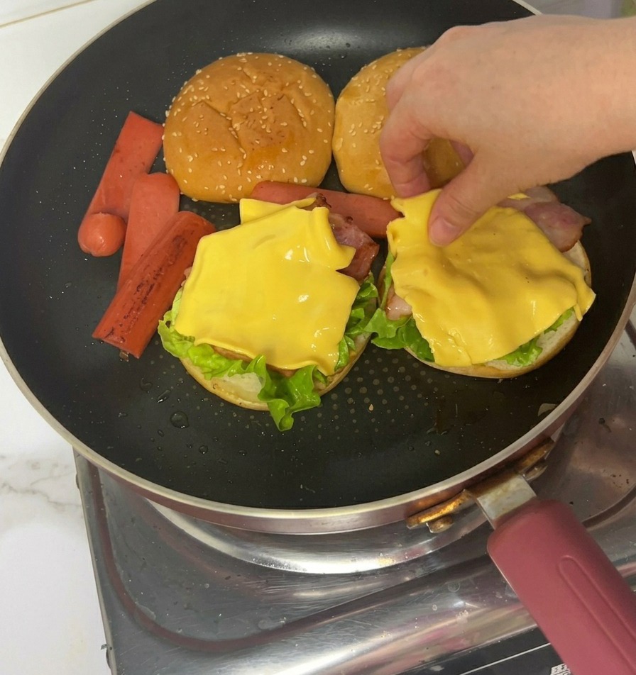 Mains utilisant des pinces pour placer des tranches de jambon cuit sur le fromage.