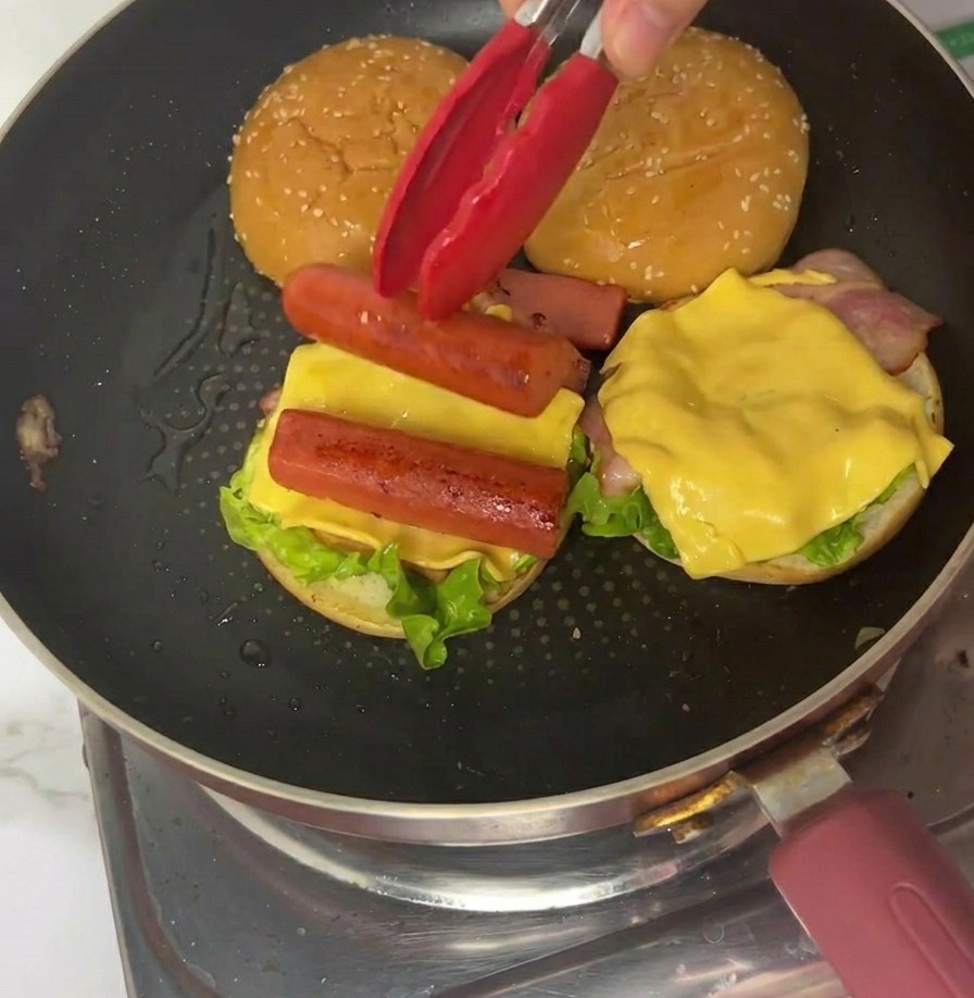 Un quartier domelette fine placé sur le montage du burger à laide de pinces rouges.