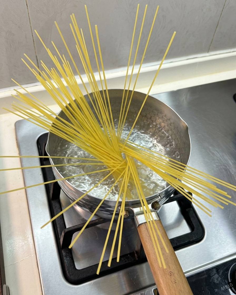Spaghettis crus partiellement immergés en éventail dans une petite casserole deau bouillante sur une cuisinière à gaz.