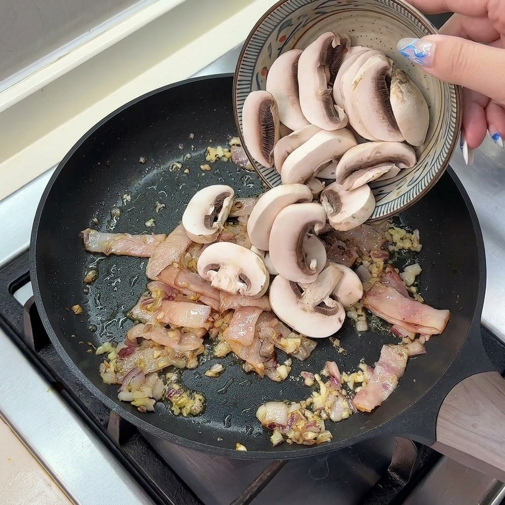 Champignons de Paris frais émincés versés dun bol en céramique dans la poêle avec les lardons et les aromates.