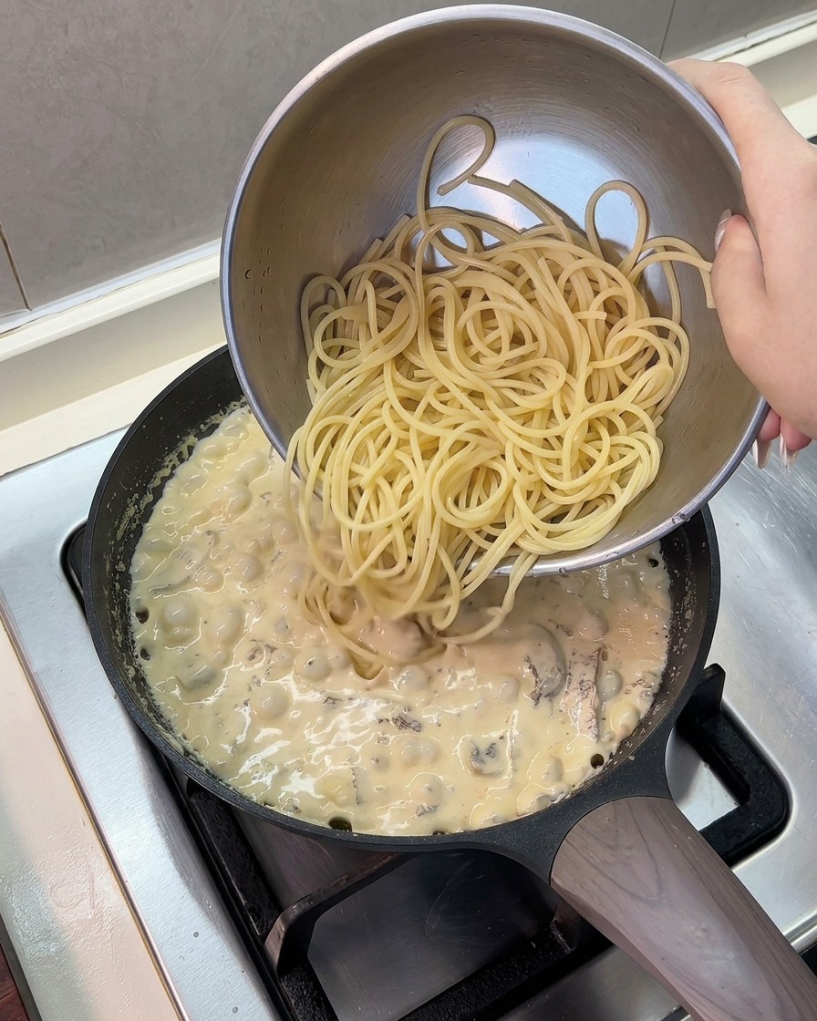 Spaghettis cuits versés depuis un saladier en inox dans la poêle de sauce frémissante.