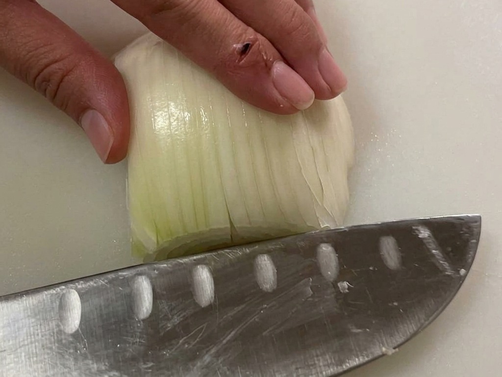 Main tenant une moitié doignon blanc sur une planche à découper avant de lémincer.