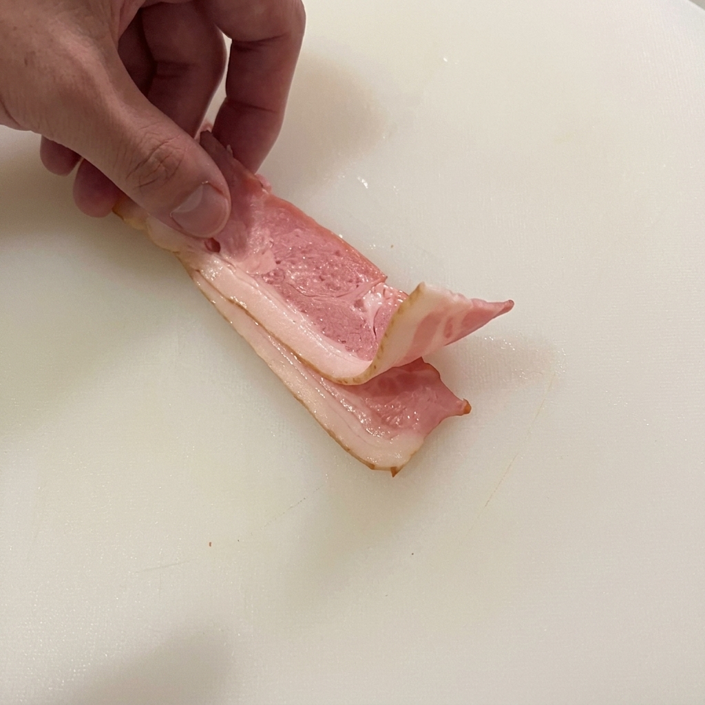Main repliant des tranches de bacon cru sur une planche à découper blanche.