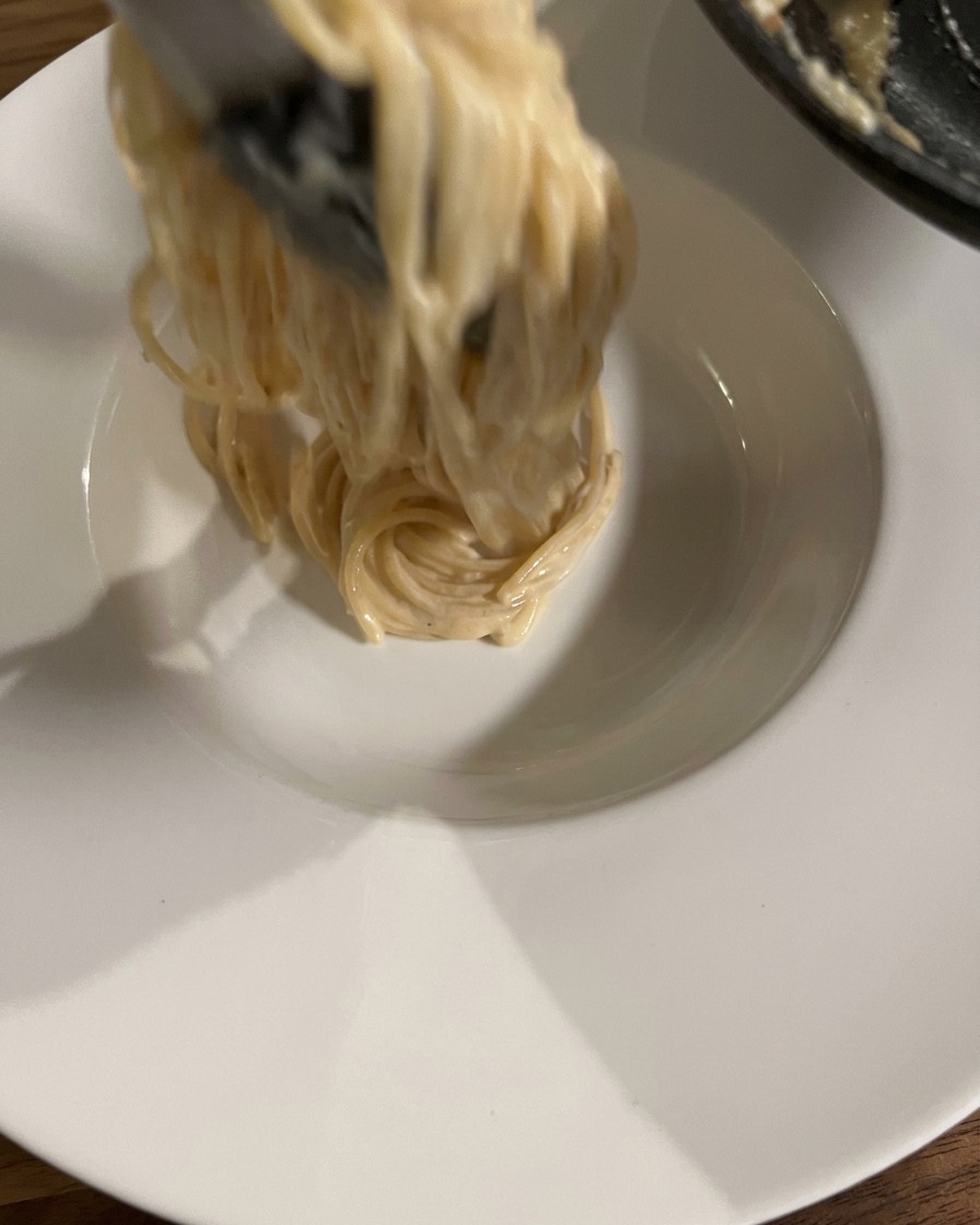 Pince soulevant et enroulant une portion de spaghetti crémeux dans un bol blanc.