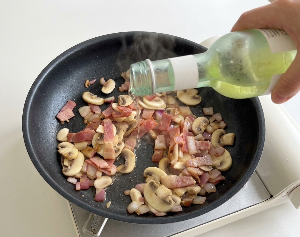Versement de vin blanc dans une poêle chaude contenant le bacon et les champignons.