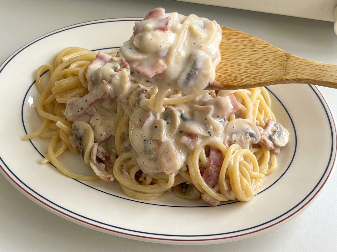 Cuillère versant le reste de sauce, bacon et champignons sur les pâtes.