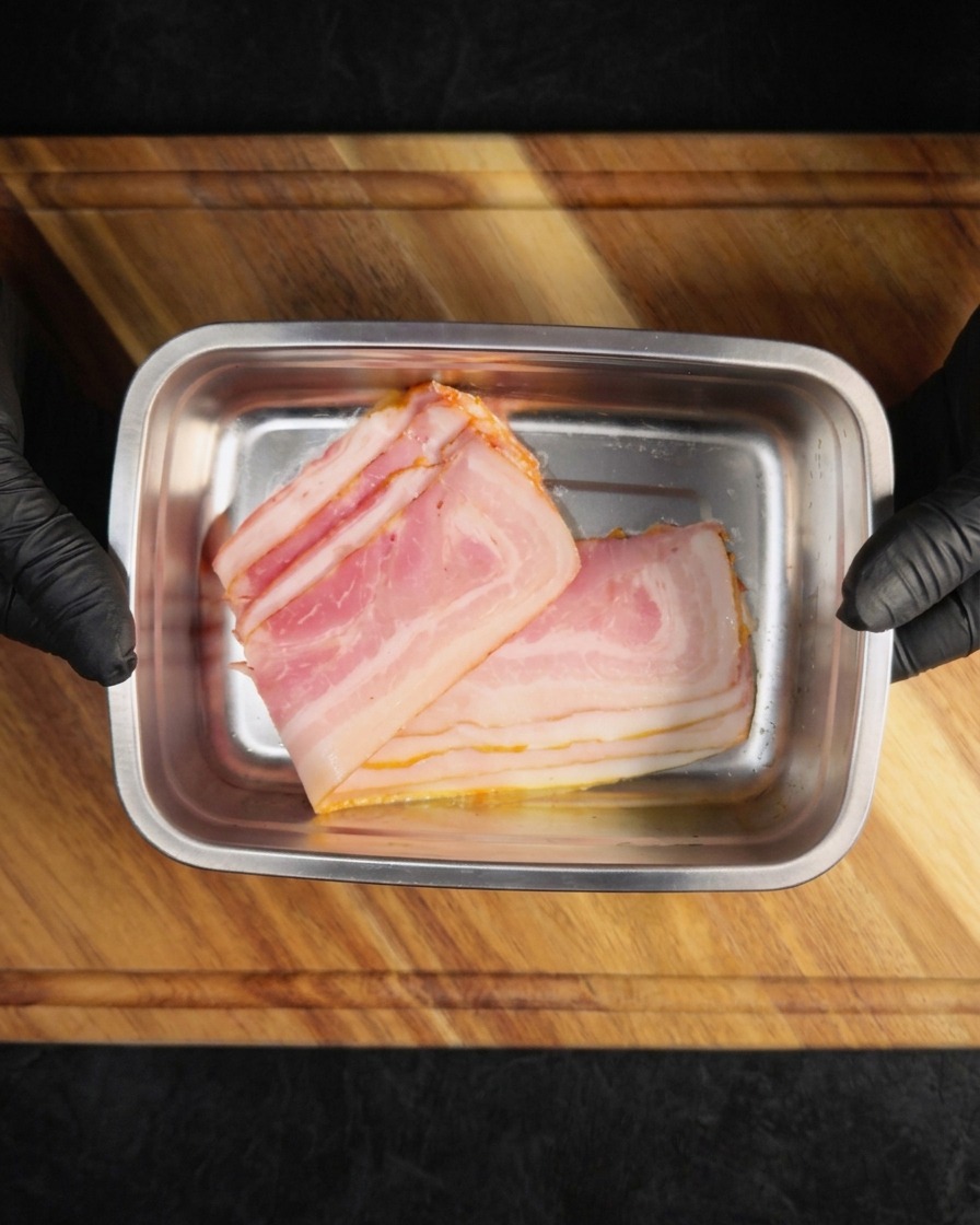 Tranches de bacon cru disposées dans un plateau métallique rectangulaire.