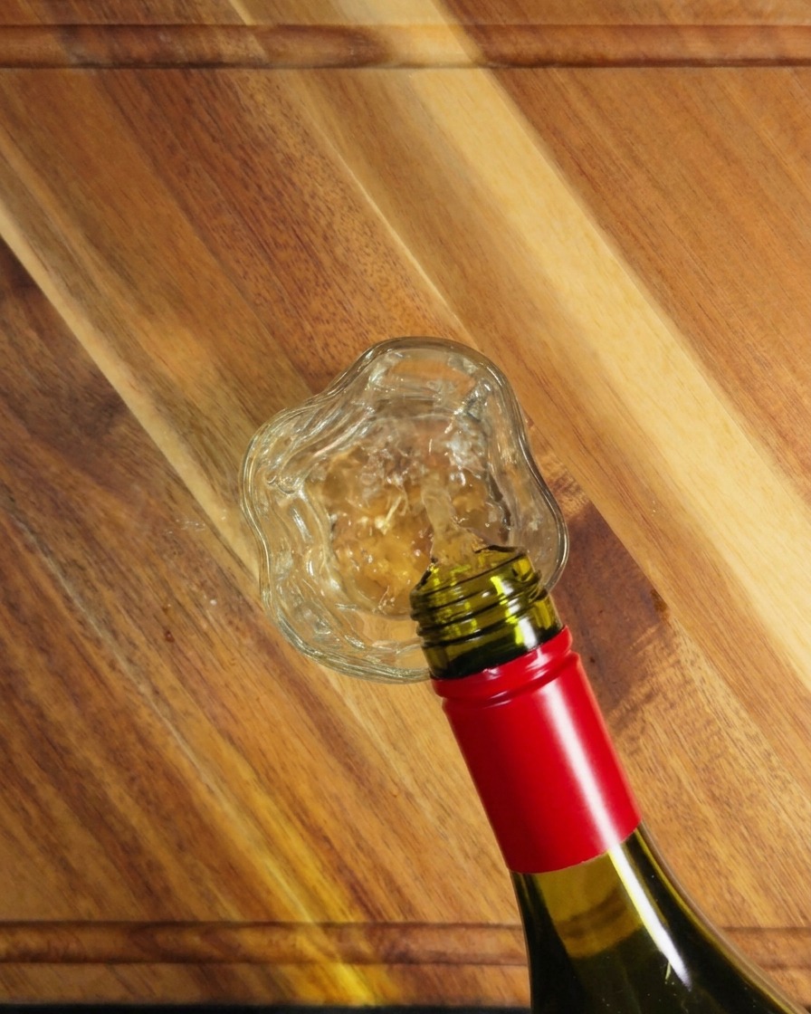 Vin blanc versé dune bouteille en verre vert dans un petit verre sur une surface en bois.