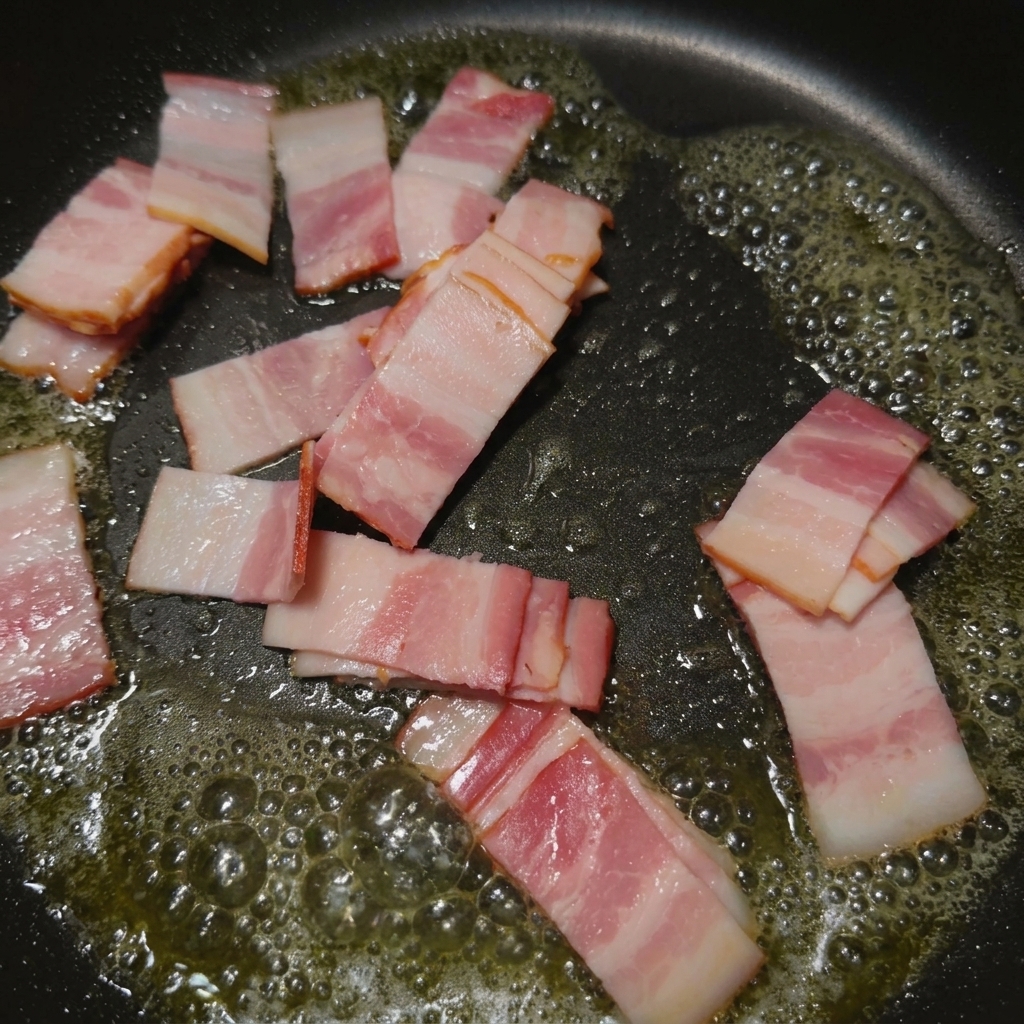 Petites lamelles de bacon grésillantes et dorées dans une poêle chaude.