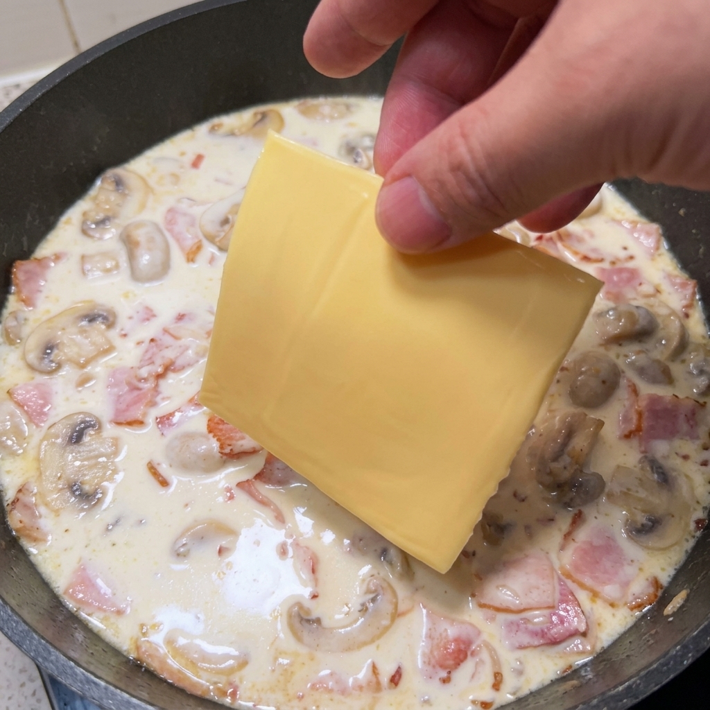Main déposant une tranche de fromage fondu sur la sauce à la crème et aux champignons.