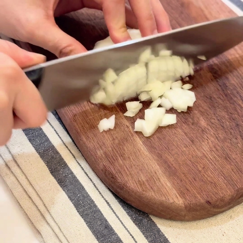 Mains coupant soigneusement un oignon blanc en petits dés réguliers.