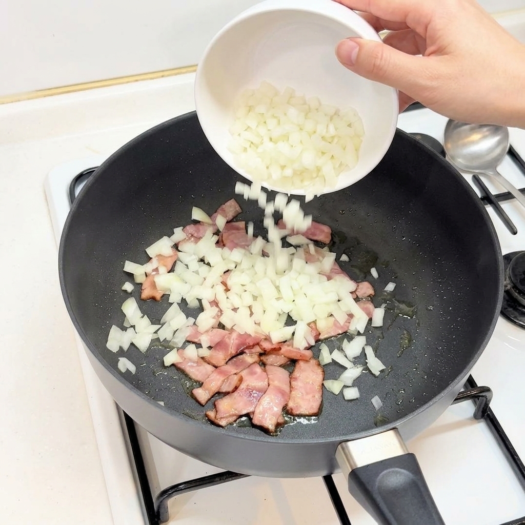 Dés doignons versés dun bol blanc dans une poêle contenant le bacon.