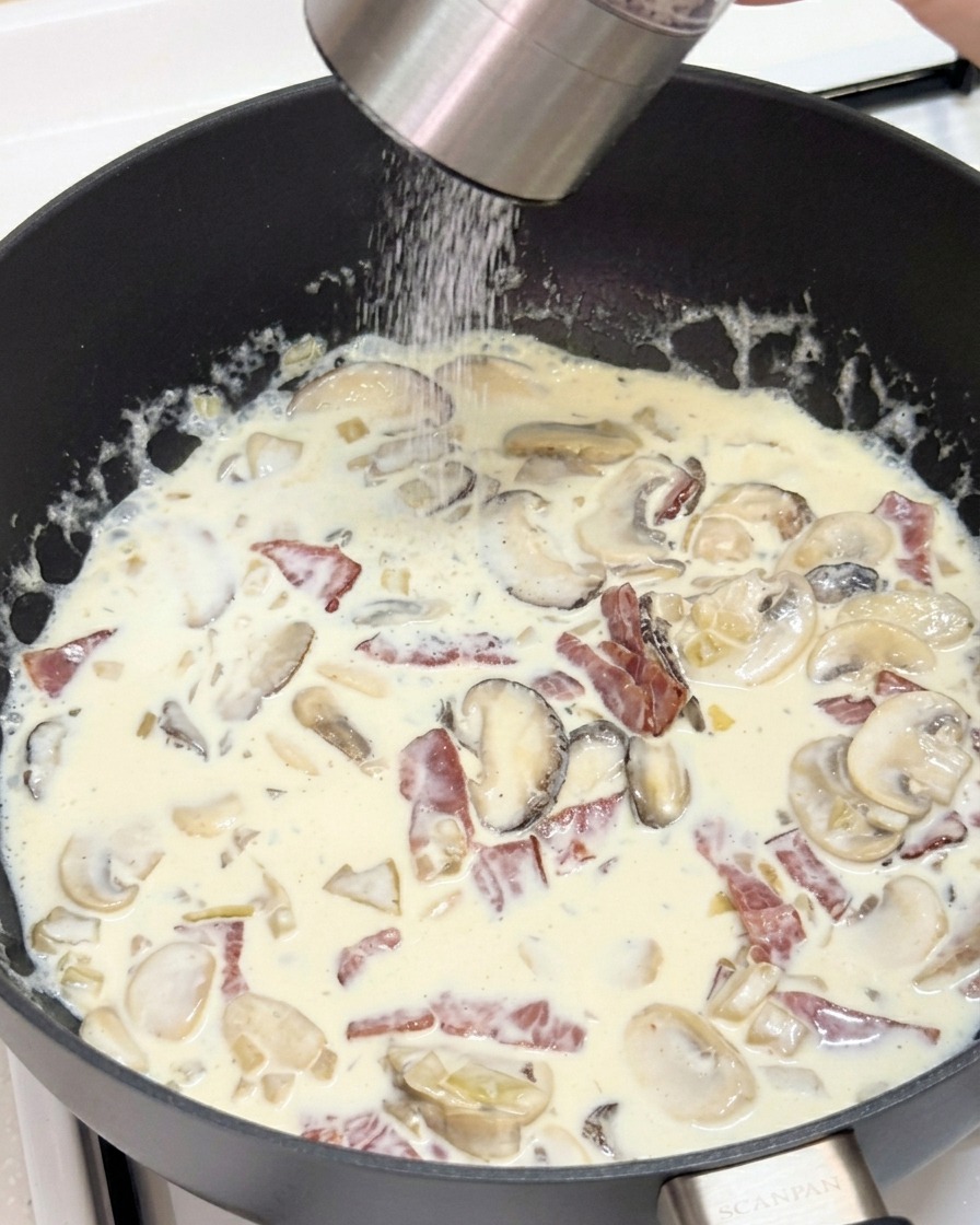 Personne utilisant un moulin à poivre au-dessus dune sauce crémeuse.