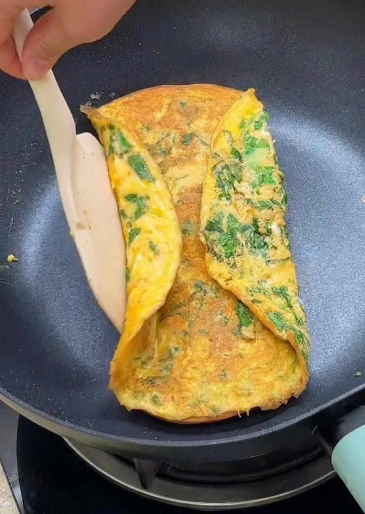 Une spatule rabattant les bords dune omelette à la laitue sur deux moitiés de pain burger toastées.