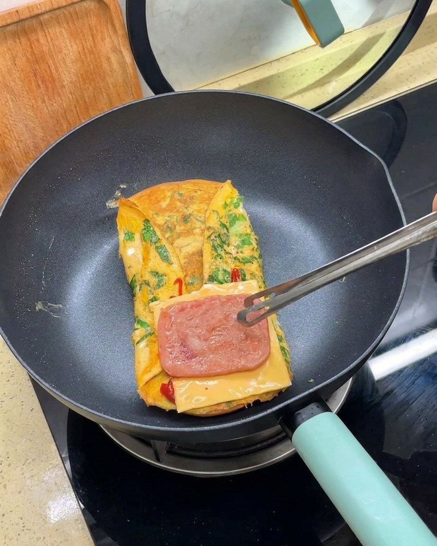 Une pince plaçant une tranche de viande cuite sur une tranche de fromage dans la poêle.