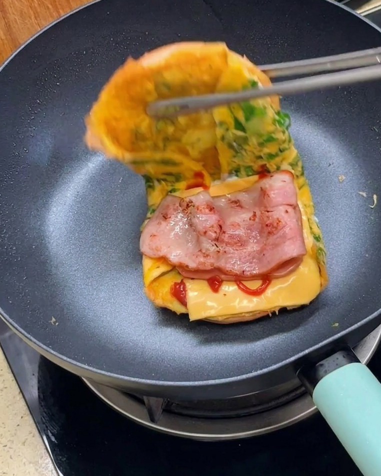 Une pince refermant les deux moitiés du burger enveloppé domelette pour former le sandwich final.