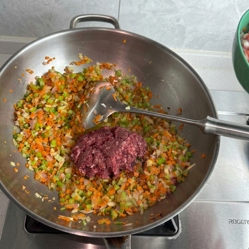Un tas de porc et de bœuf hachés crus posé sur un lit de légumes sautés dans un wok en inox.