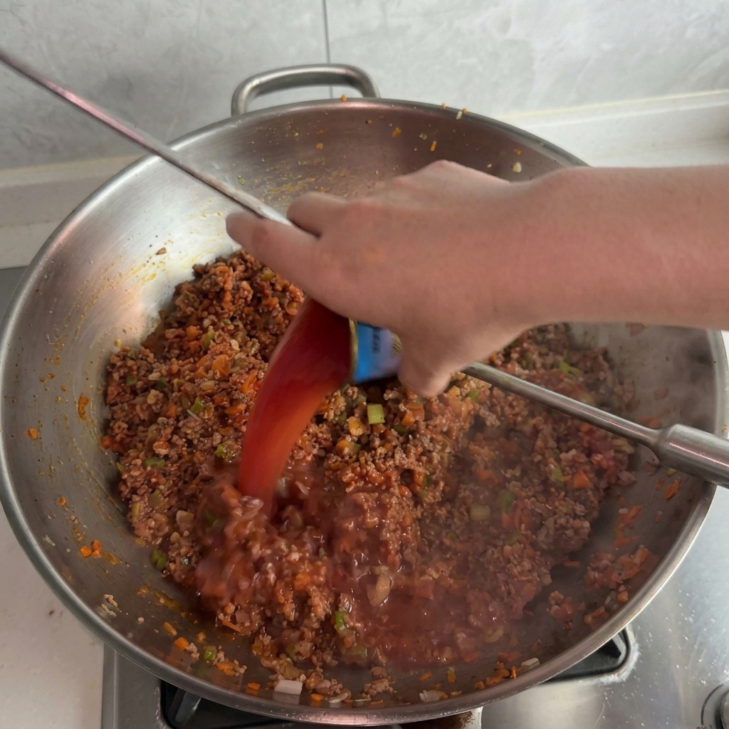 De leau teintée de tomate versée dune petite boîte de conserve dans un wok bouillonnant.