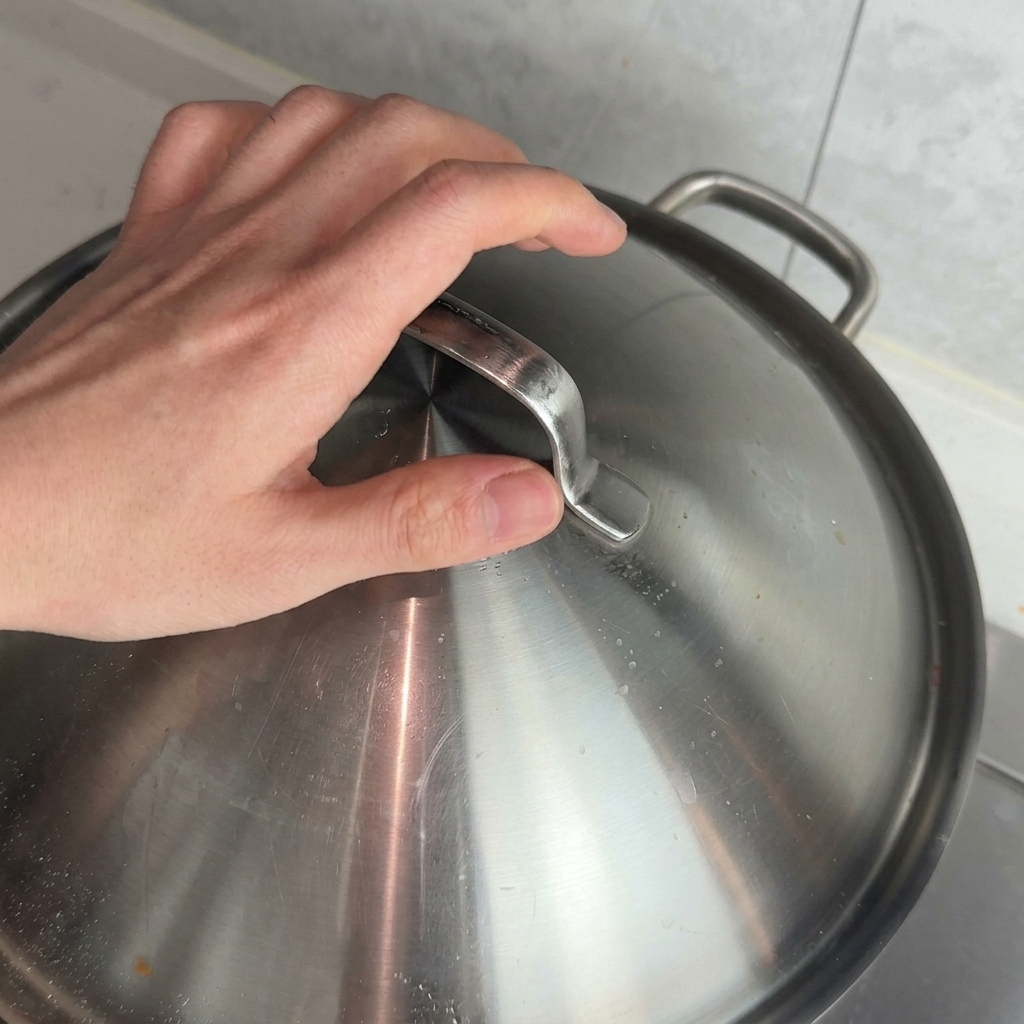 Une main plaçant un couvercle en métal sur une casserole pour laisser mijoter la sauce bolognaise.