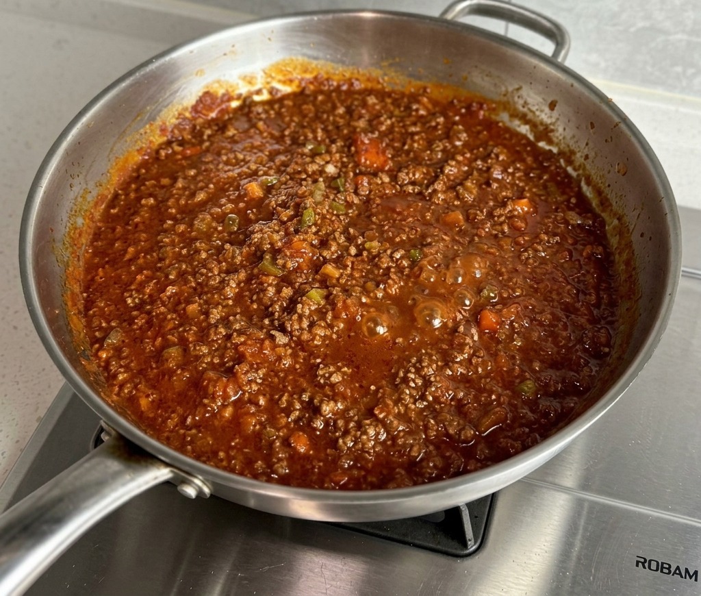 Sauce bolognaise épaisse et bouillonnante mijotant dans une poêle en inox.