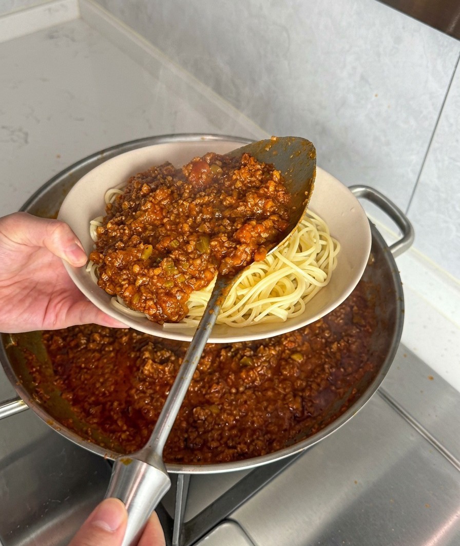 Une généreuse louche de sauce bolognaise épaisse versée sur un bol de spaghettis frais.